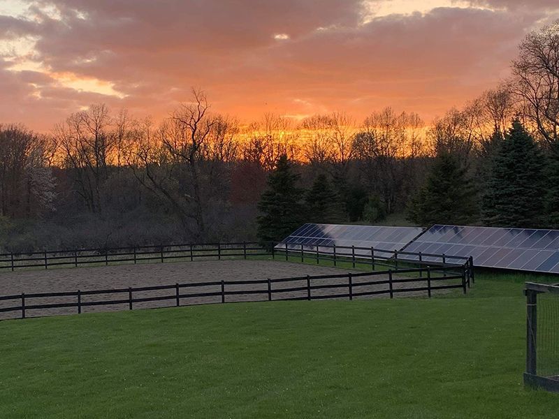 Sunset over a horse arena and solar panels, with trees in the background.