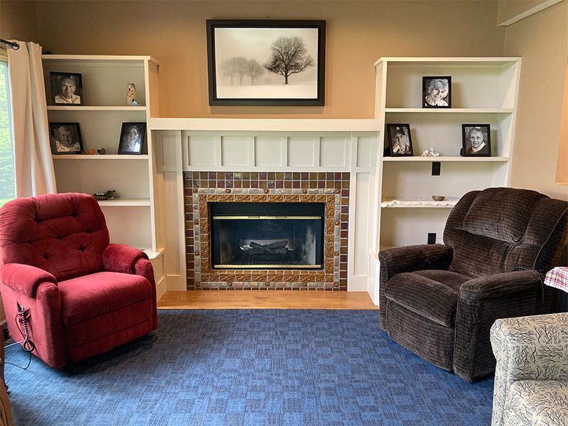 Living room with fireplace, bookshelves, and two recliners. Blue carpet, red and brown chairs.