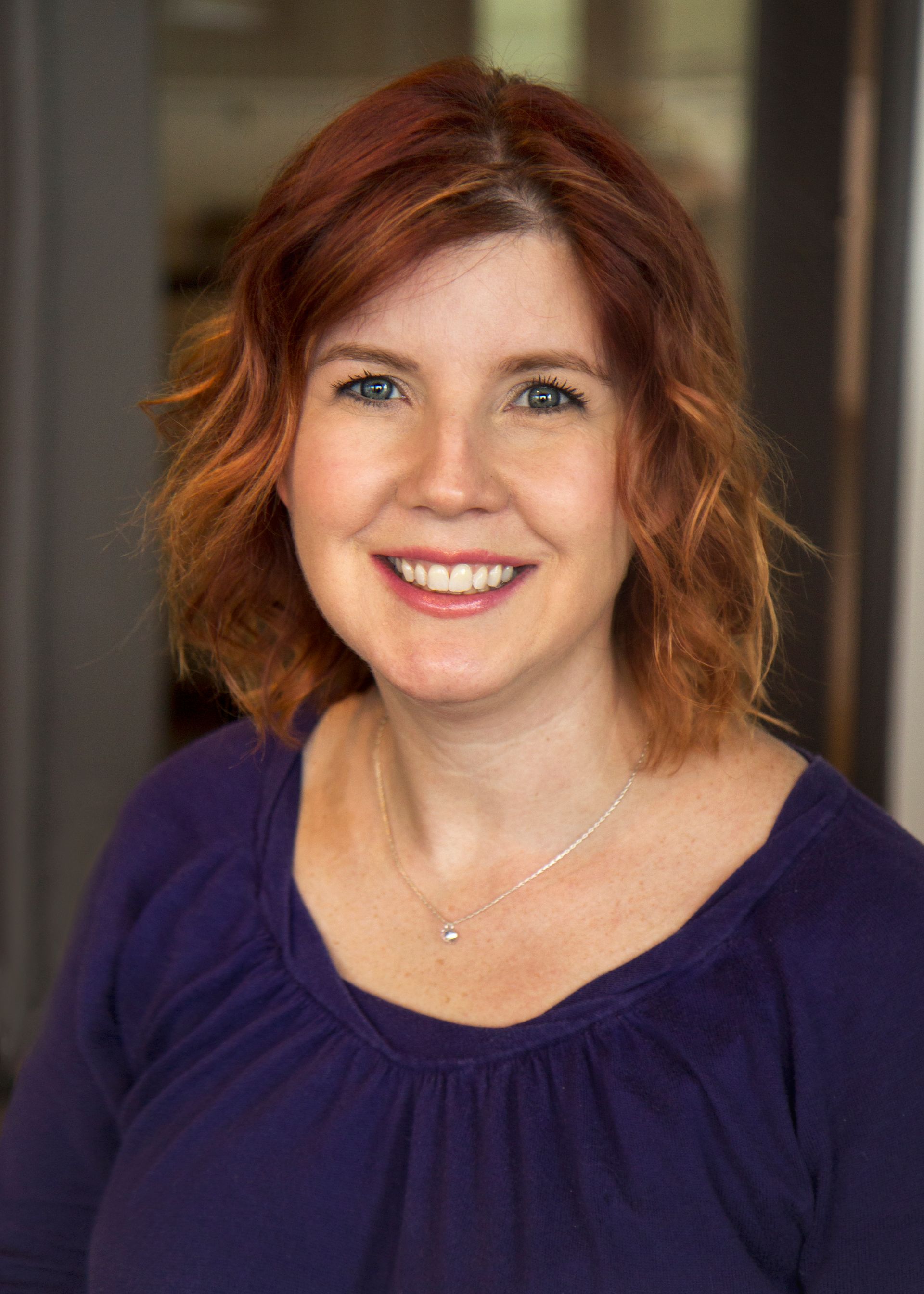 Woman with red hair and a purple shirt smiles.