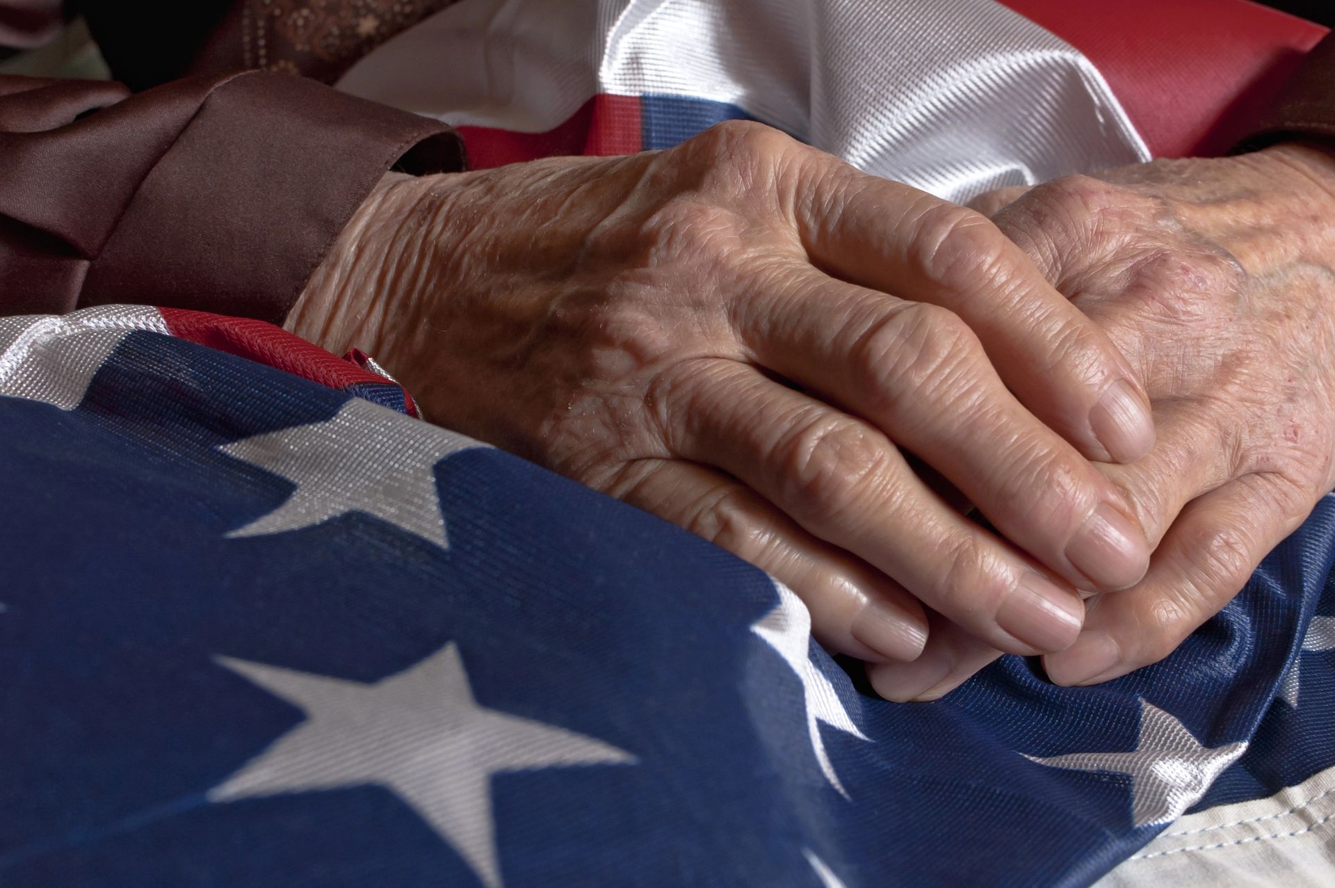 Hands of an elderly person resting on an American flag, folded.