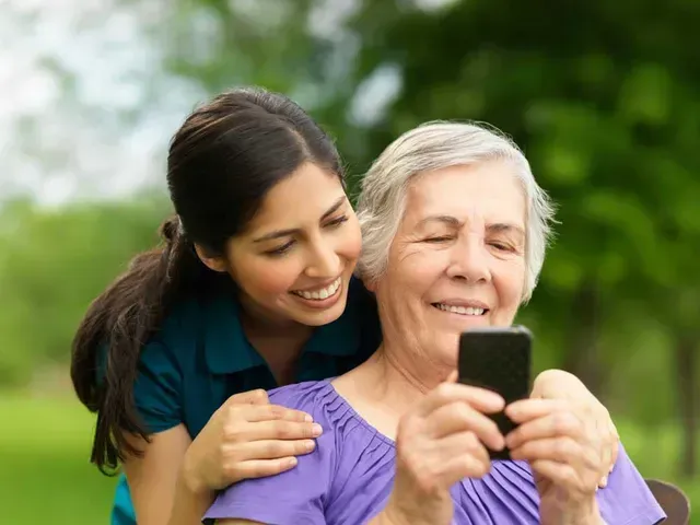 An older woman holding a cellphone with a younger woman leaning over her shoulder.