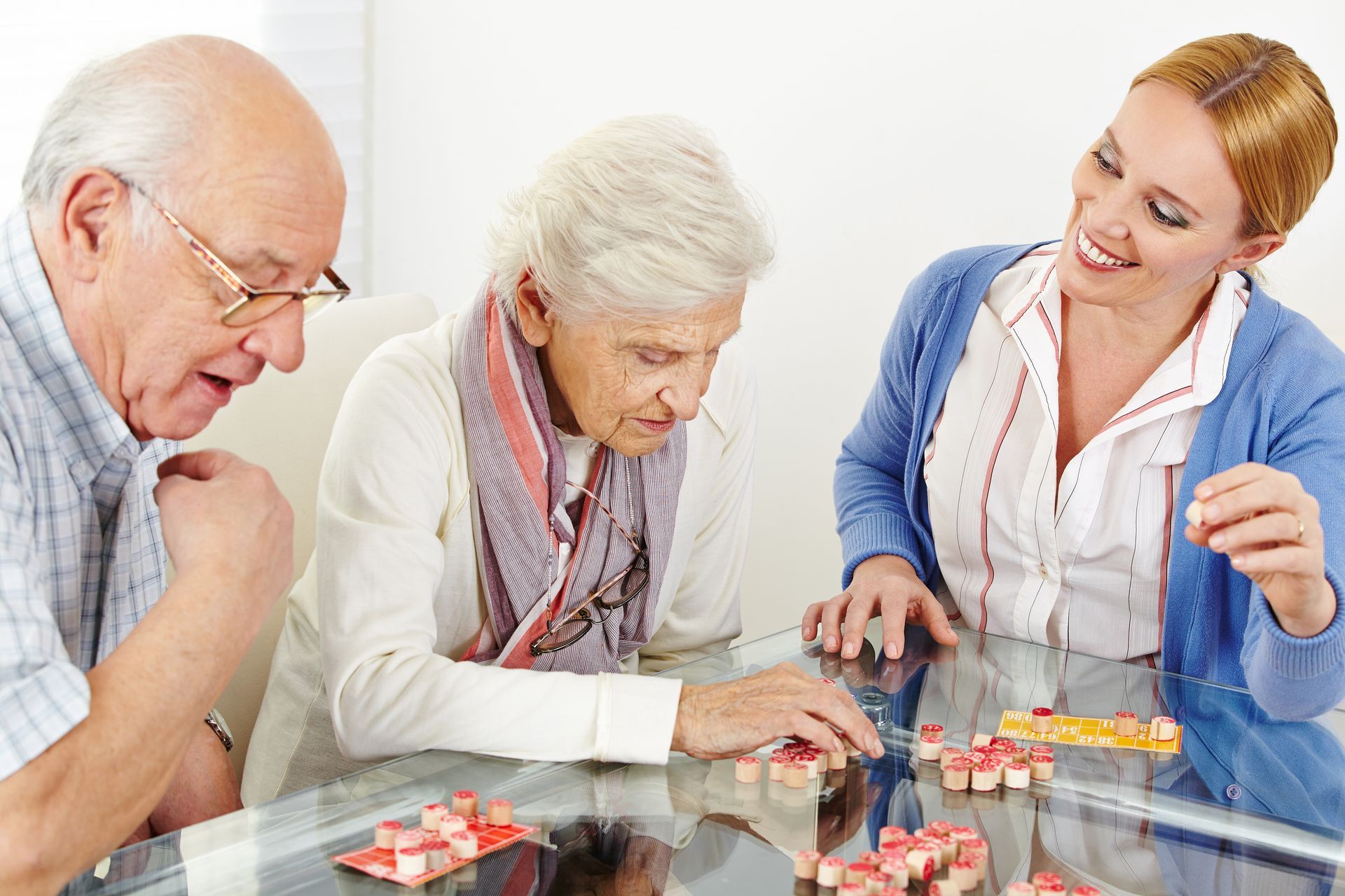 An older couple and a woman play a board game, smiling, at a glass table.