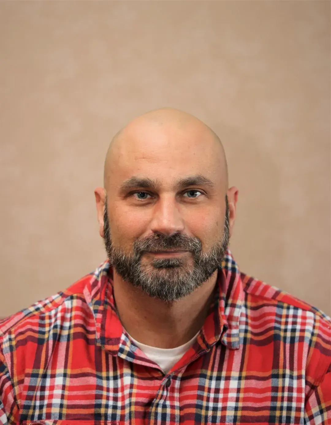 Bald man with beard wearing red plaid shirt, smiling at camera.