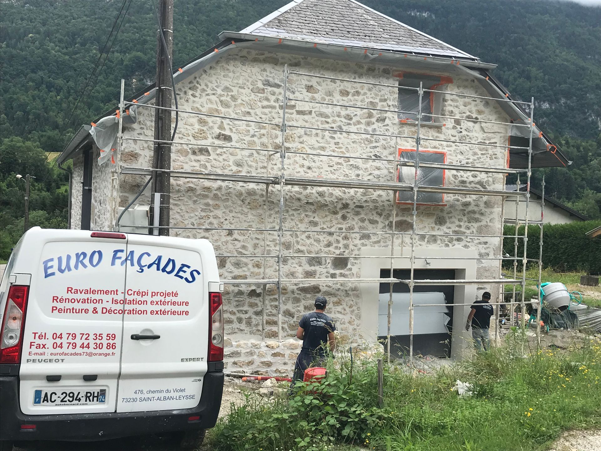 une camionnette blanche d'euro façade est garée devant un bâtiment en pierre dont la façade en pierre est actuellement en cours.