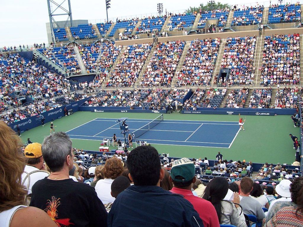 Tennis match in a packed stadium. Players on court; crowd watches from blue seats.