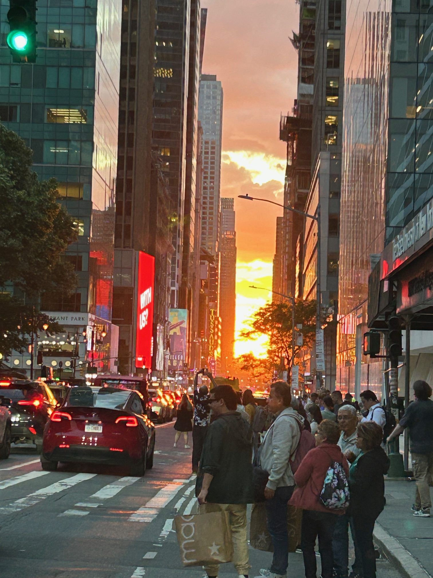 Sunset illuminates a busy New York City street with tall buildings and crowds of people.