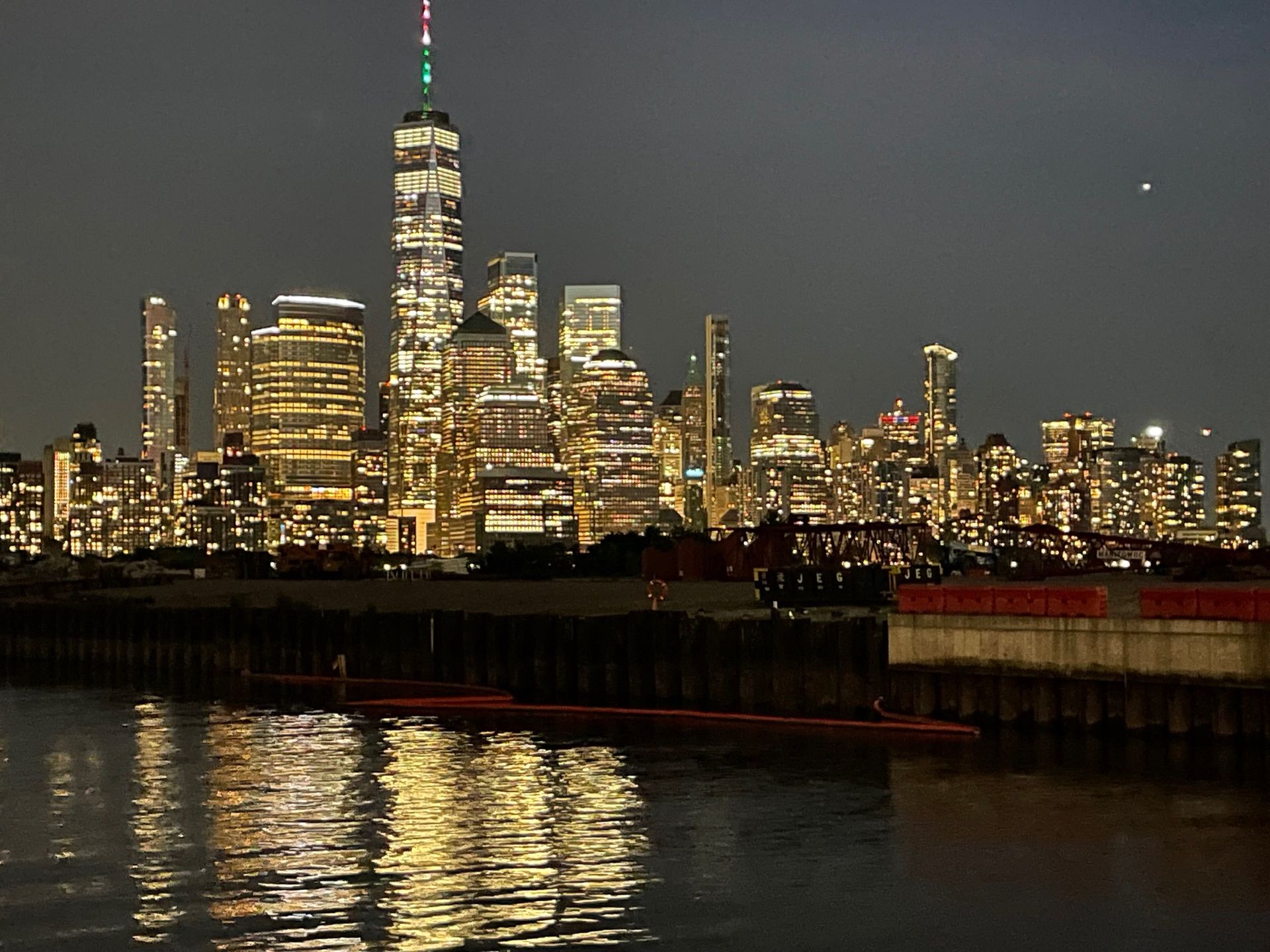 Night view of NYC skyline with illuminated buildings reflecting in the water.