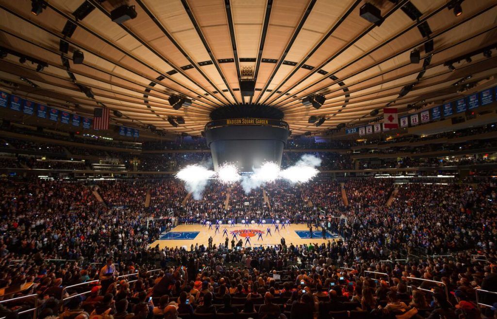 Basketball game in Madison Square Garden, filled with fans. Center court action with stage lights.