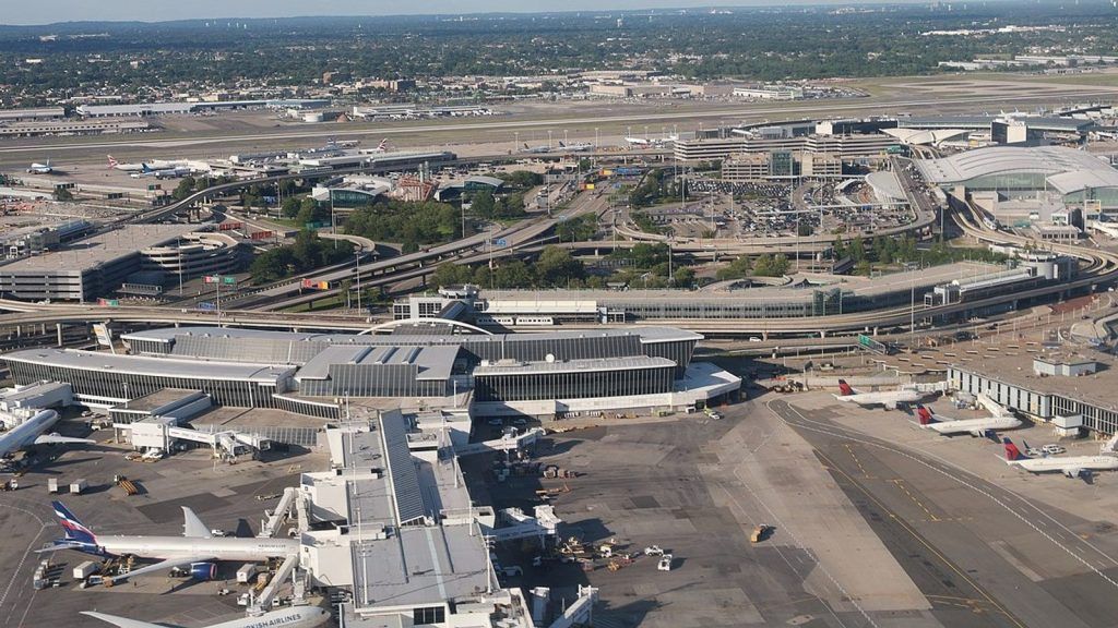 Aerial view of an airport with airplanes parked at gates, runways, and terminal buildings, under a blue sky.
