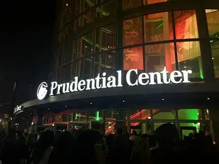Prudential Center sign illuminated at night, with people gathered in front of the building.