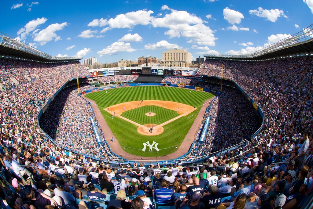 Yankee Stadium, packed with fans, bright blue sky above. Baseball field in the center.