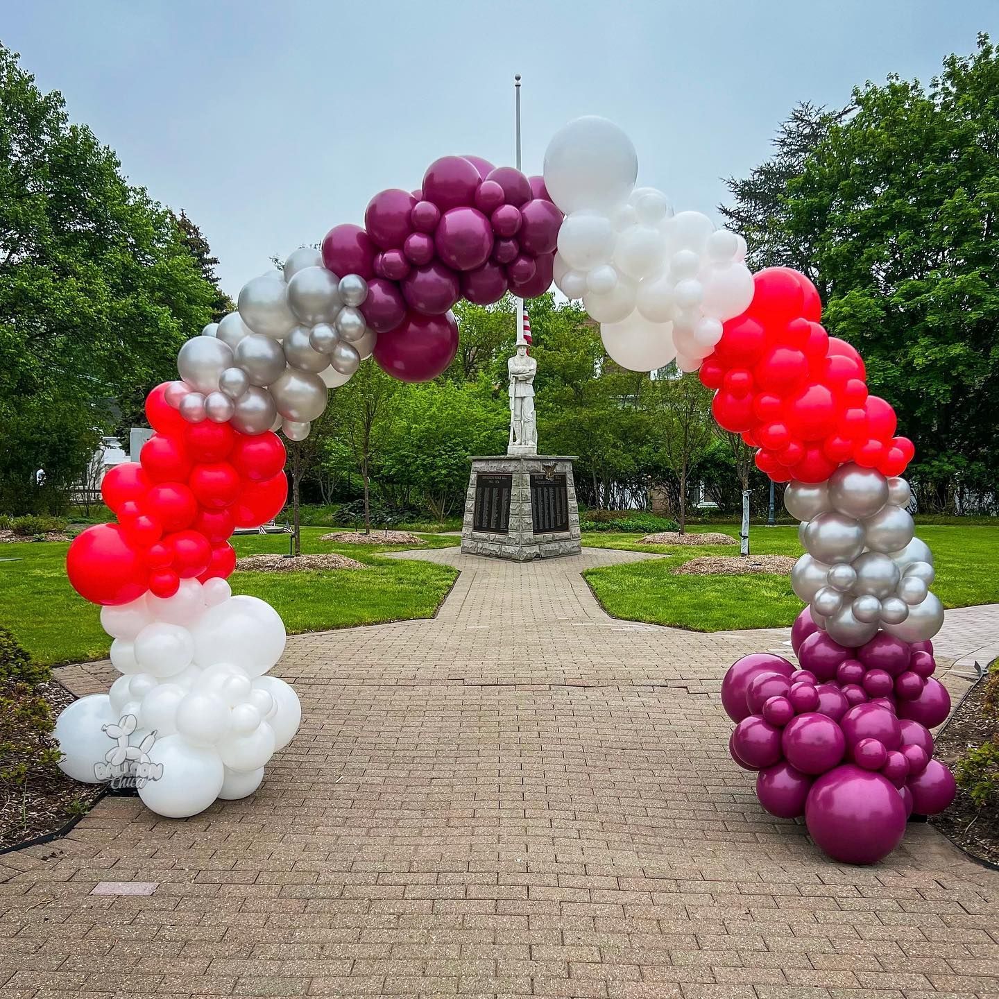 a red , white and purple balloon arch in a park