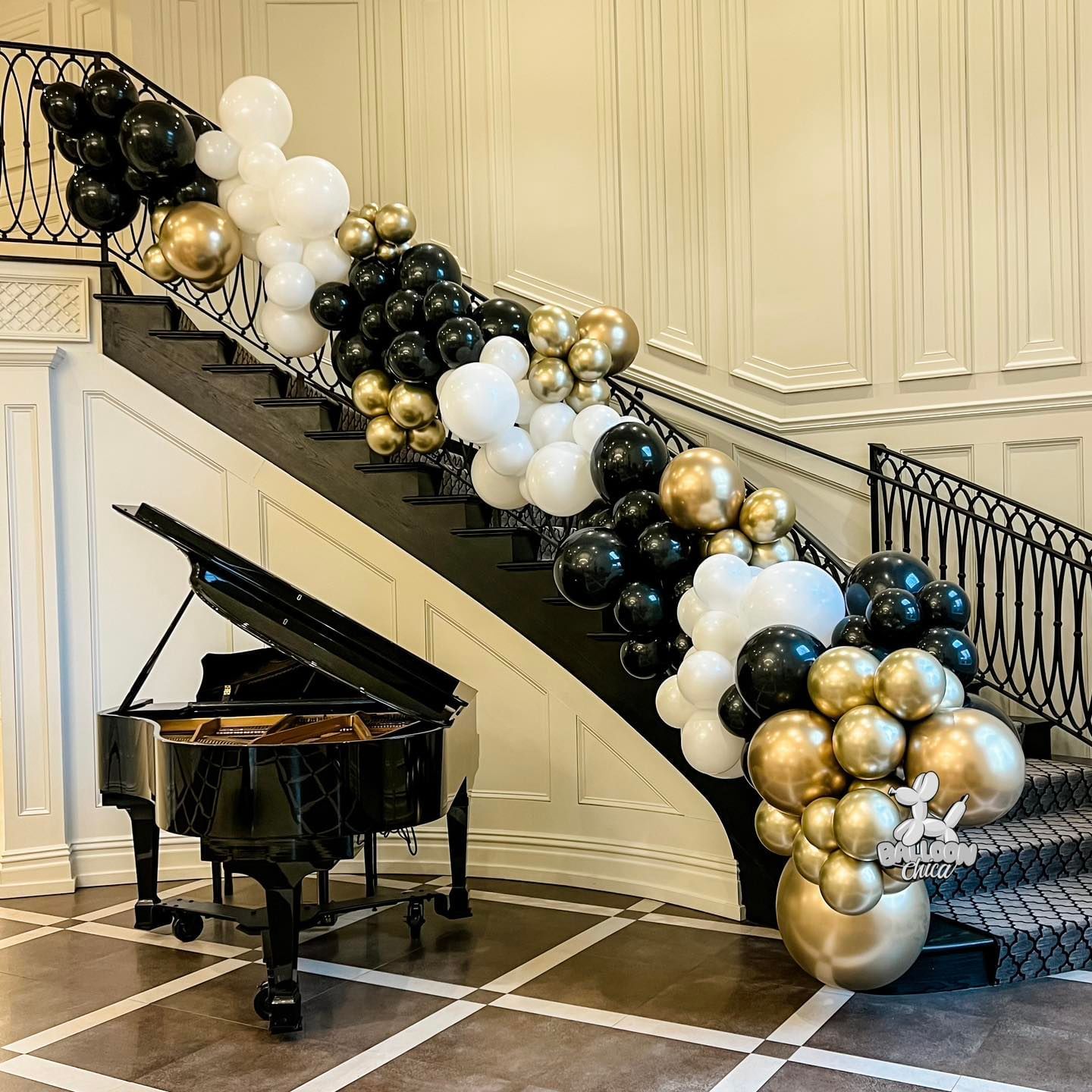 a piano is sitting next to a staircase decorated with black , white and gold balloons