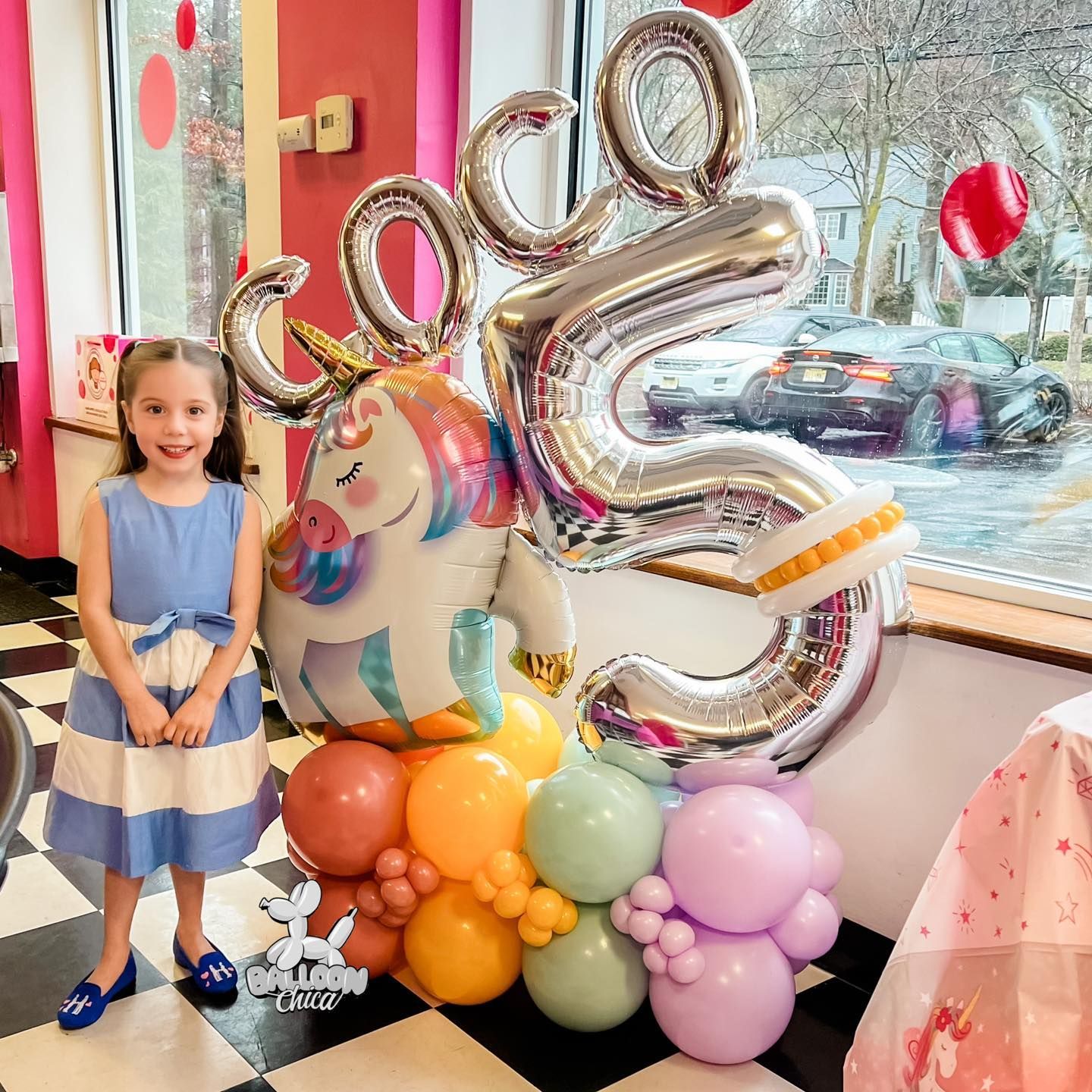a little girl is standing next to a bunch of balloons
