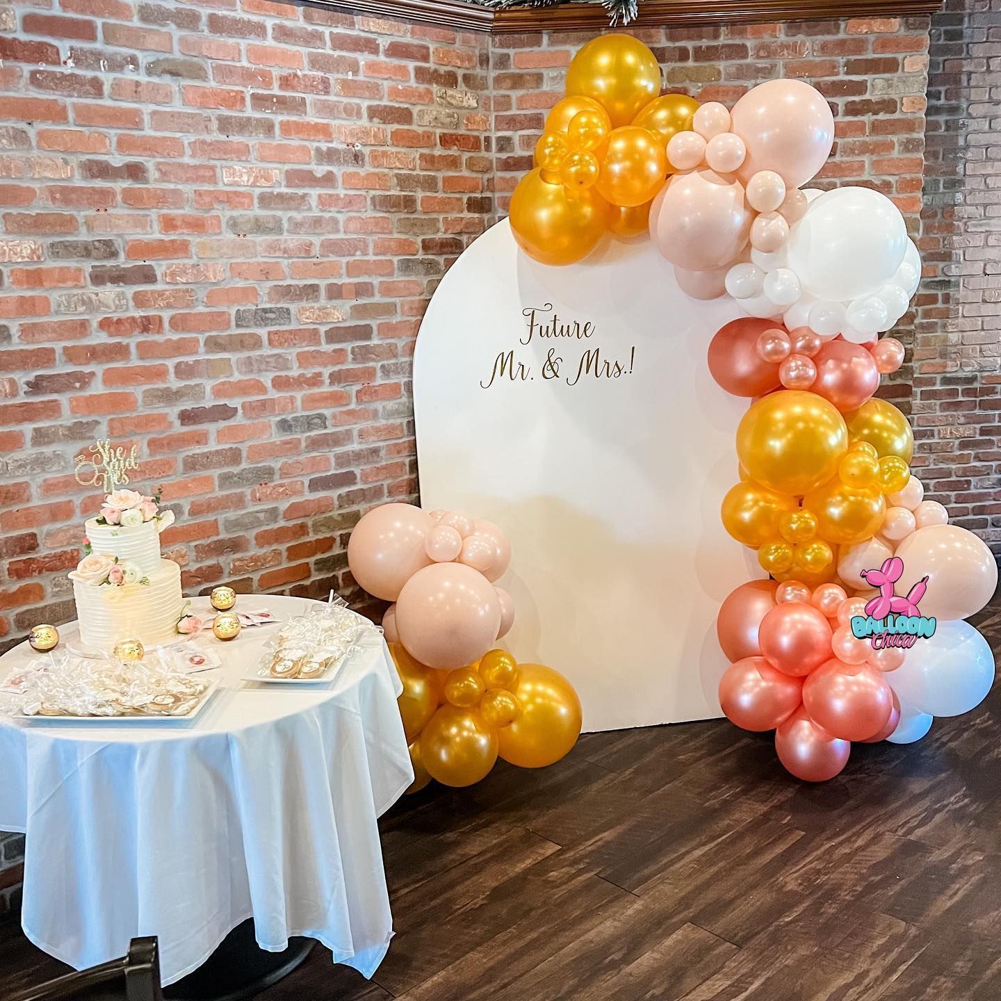 a table with a cake and balloons in front of a brick wall