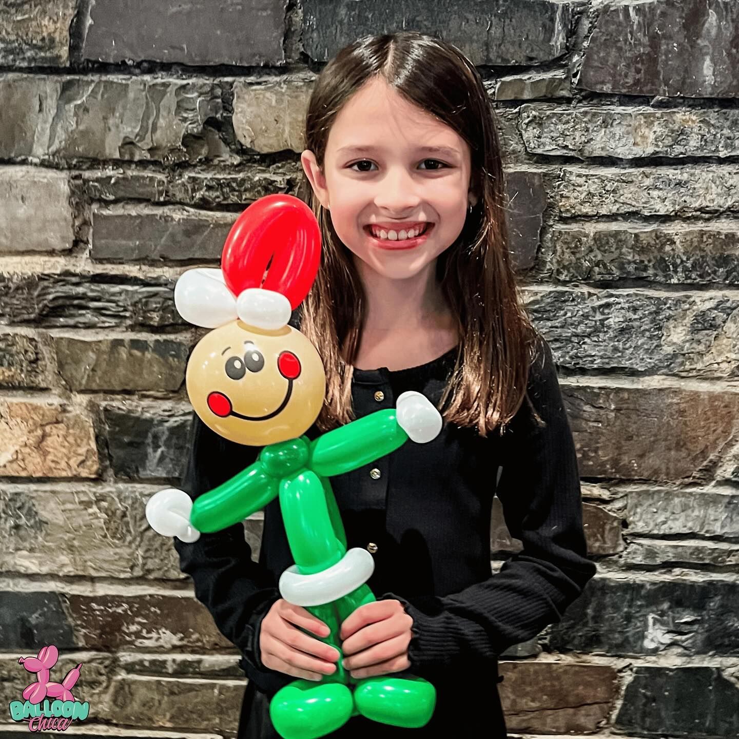 a young girl is holding a balloon elf in front of a brick wall