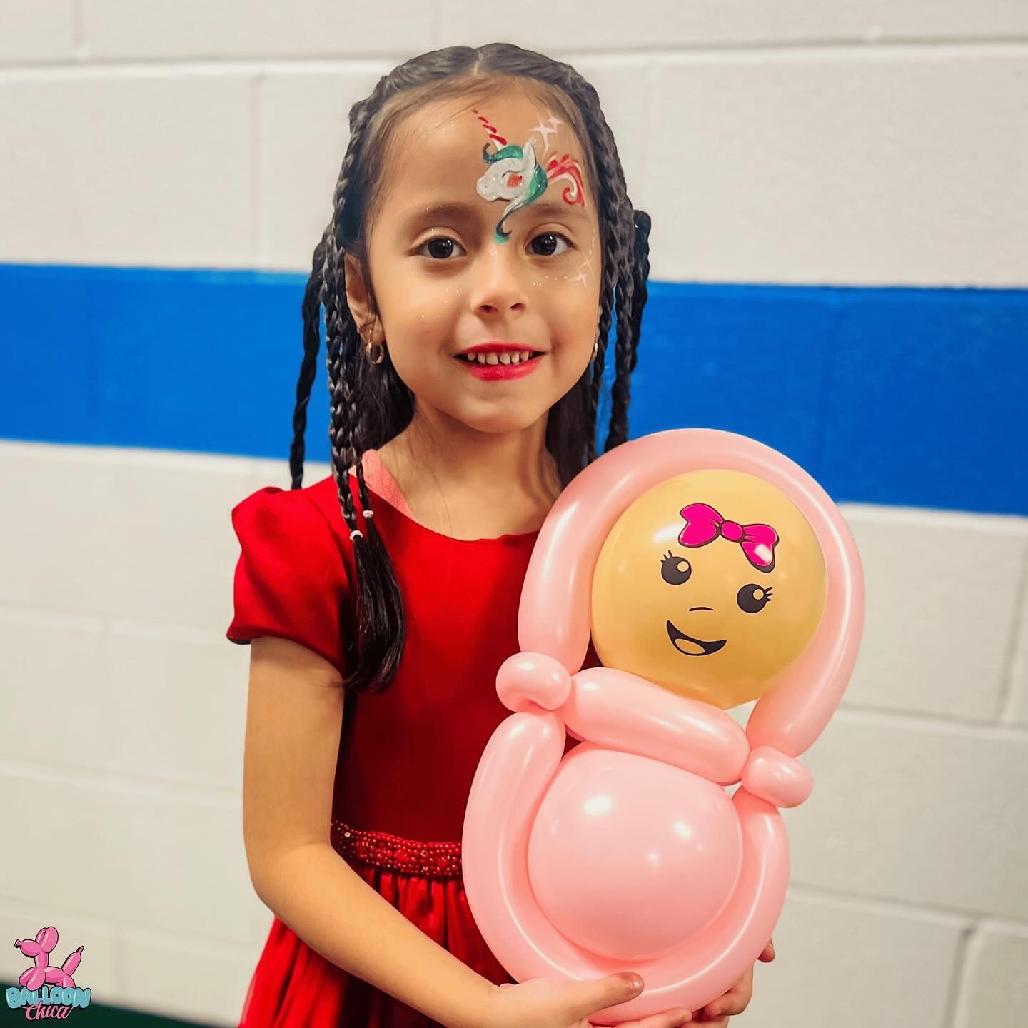 a little girl in a red dress is holding a pink balloon doll