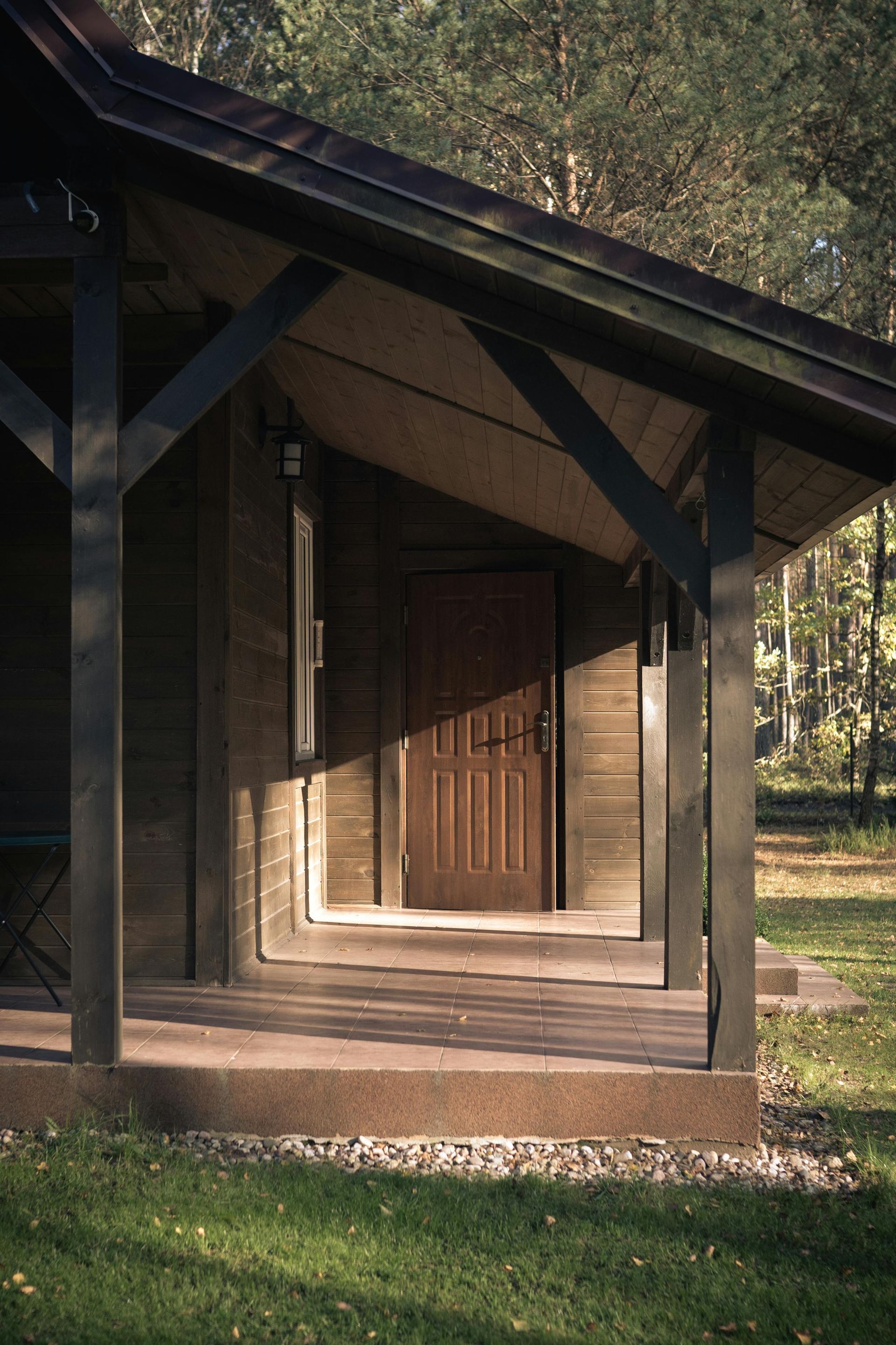 Wooden cabin porch with brown door, shadowed entry, and green grass.