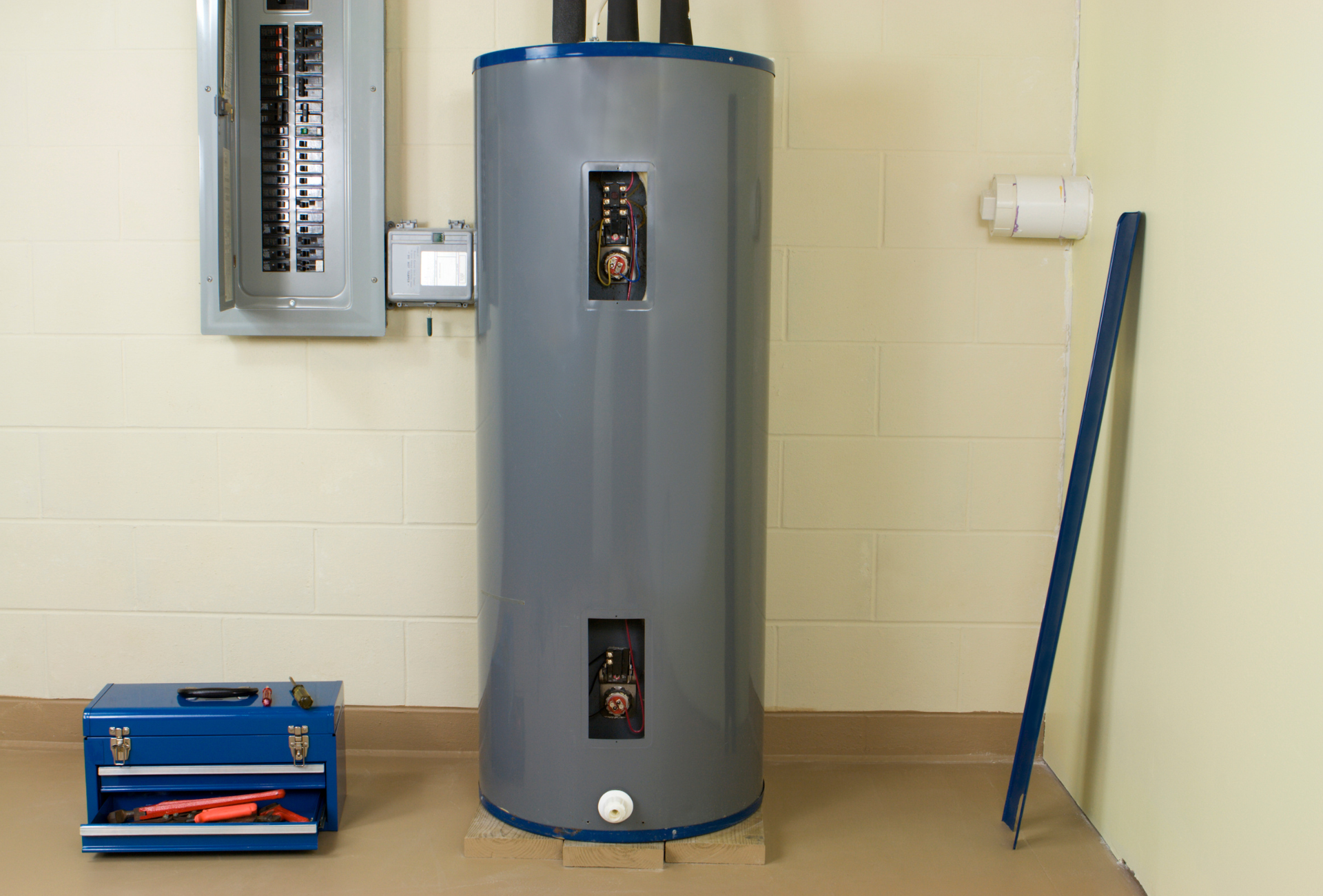 A water heater is sitting in a room next to a toolbox.