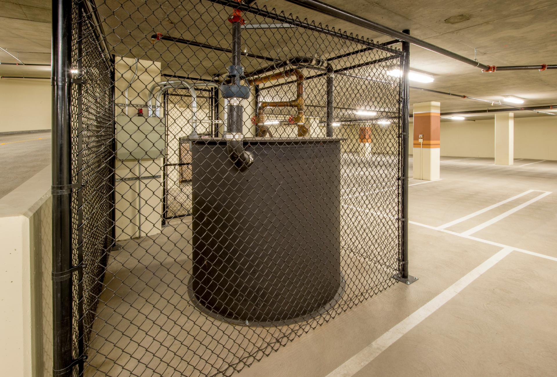 A large black tank is behind a chain link fence in a parking garage