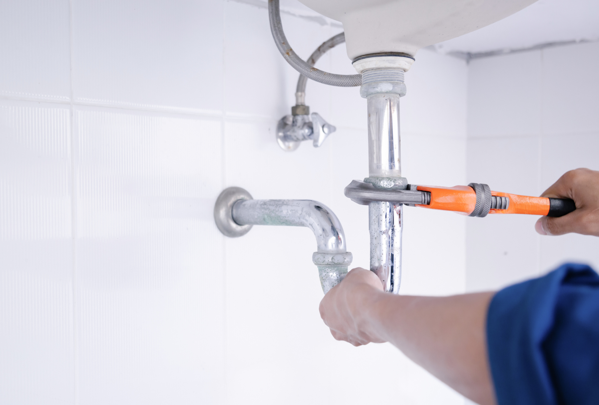 A plumber is fixing a sink pipe with a wrench.