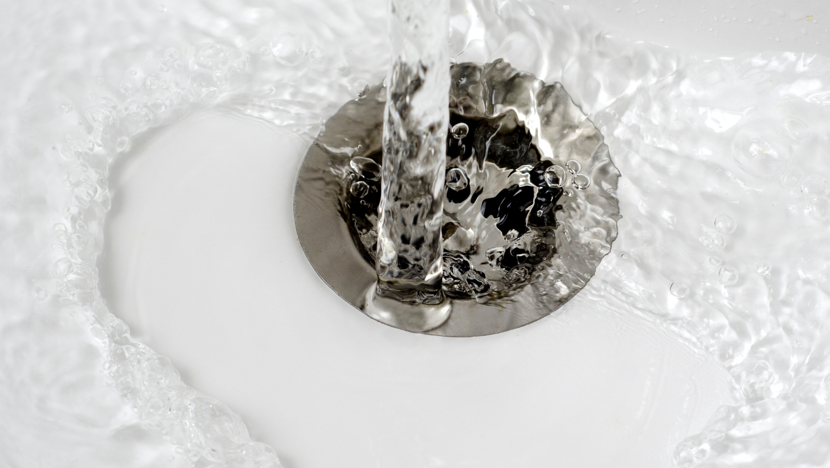 Water is running down a drain in a bathroom sink.