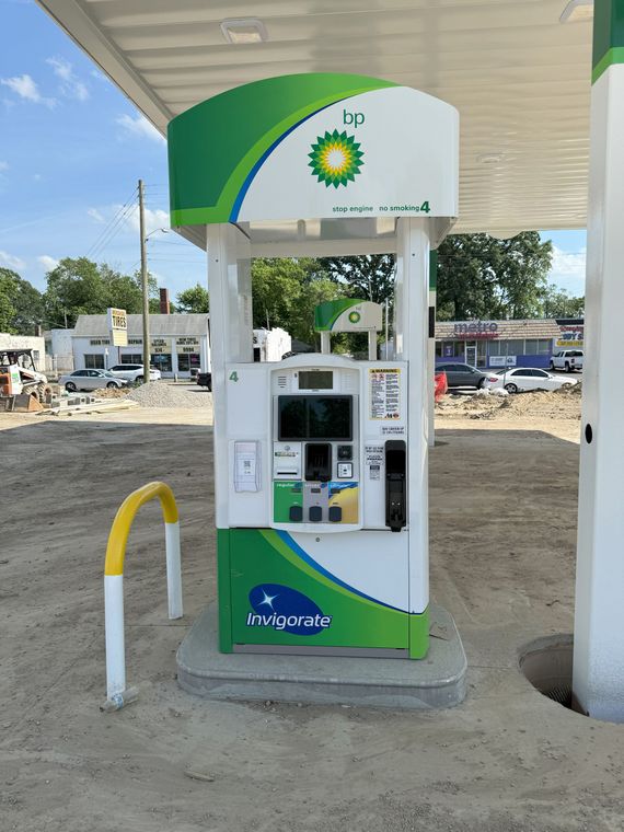 A BP gas pump with a green and white design, set on a concrete pad under a canopy, in an outdoor setting.
