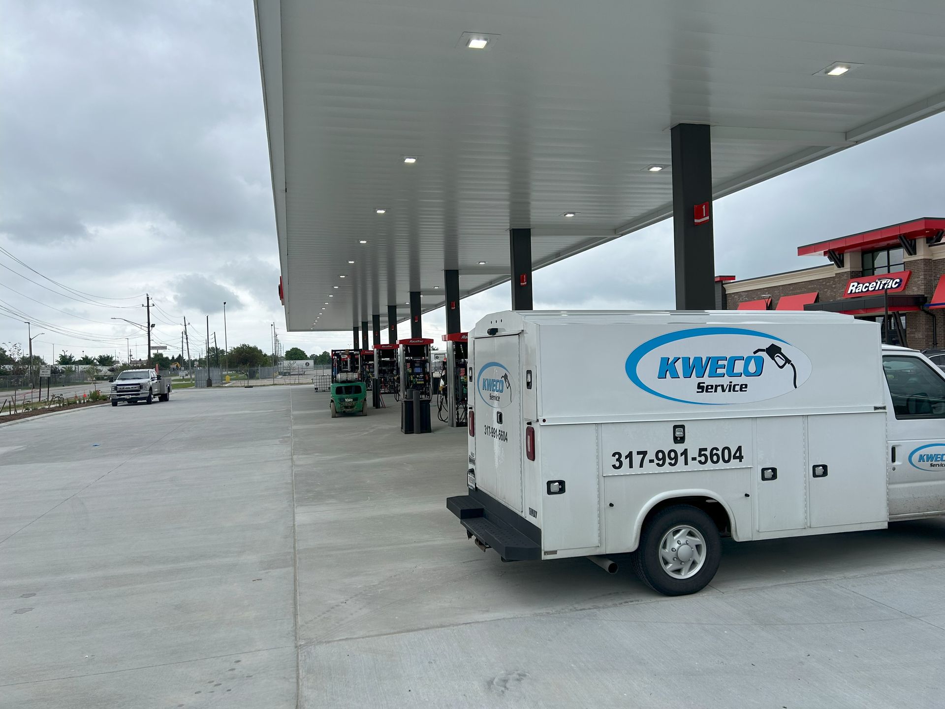 A white KMECO service truck parked at a gas station under a canopy. The sky is overcast.