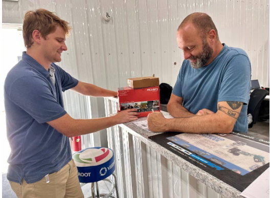 Two men looking at product on a counter; one man holds a box. Indoor setting, neutral colors.