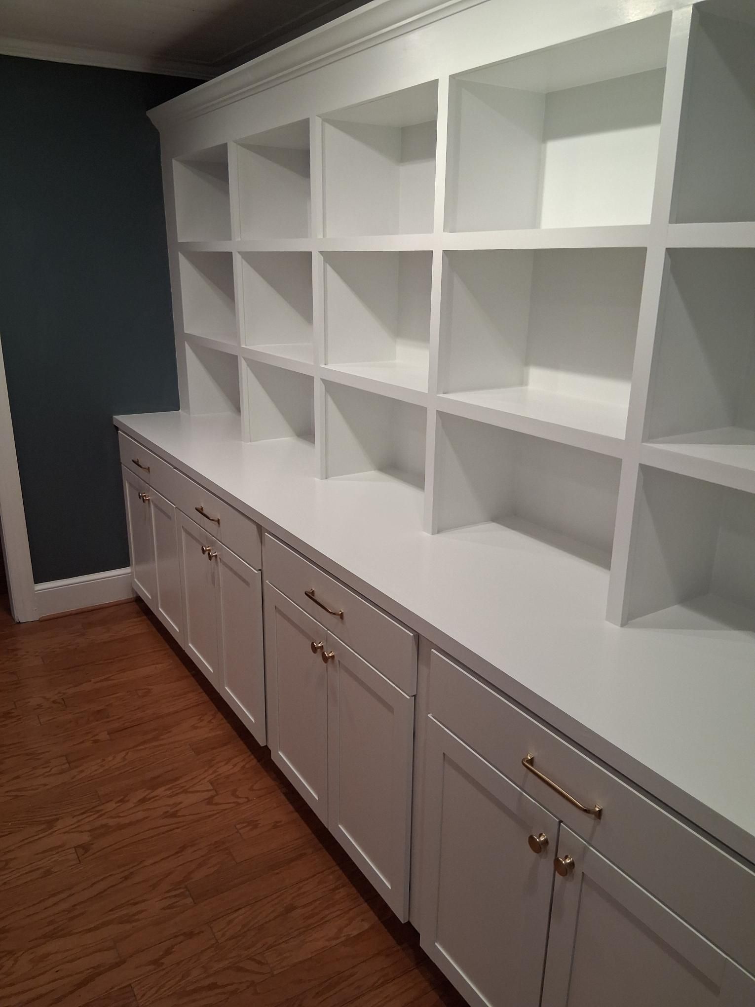 White floor-to-ceiling built-in shelving unit with lower cabinets and drawers, positioned against a dark blue wall.