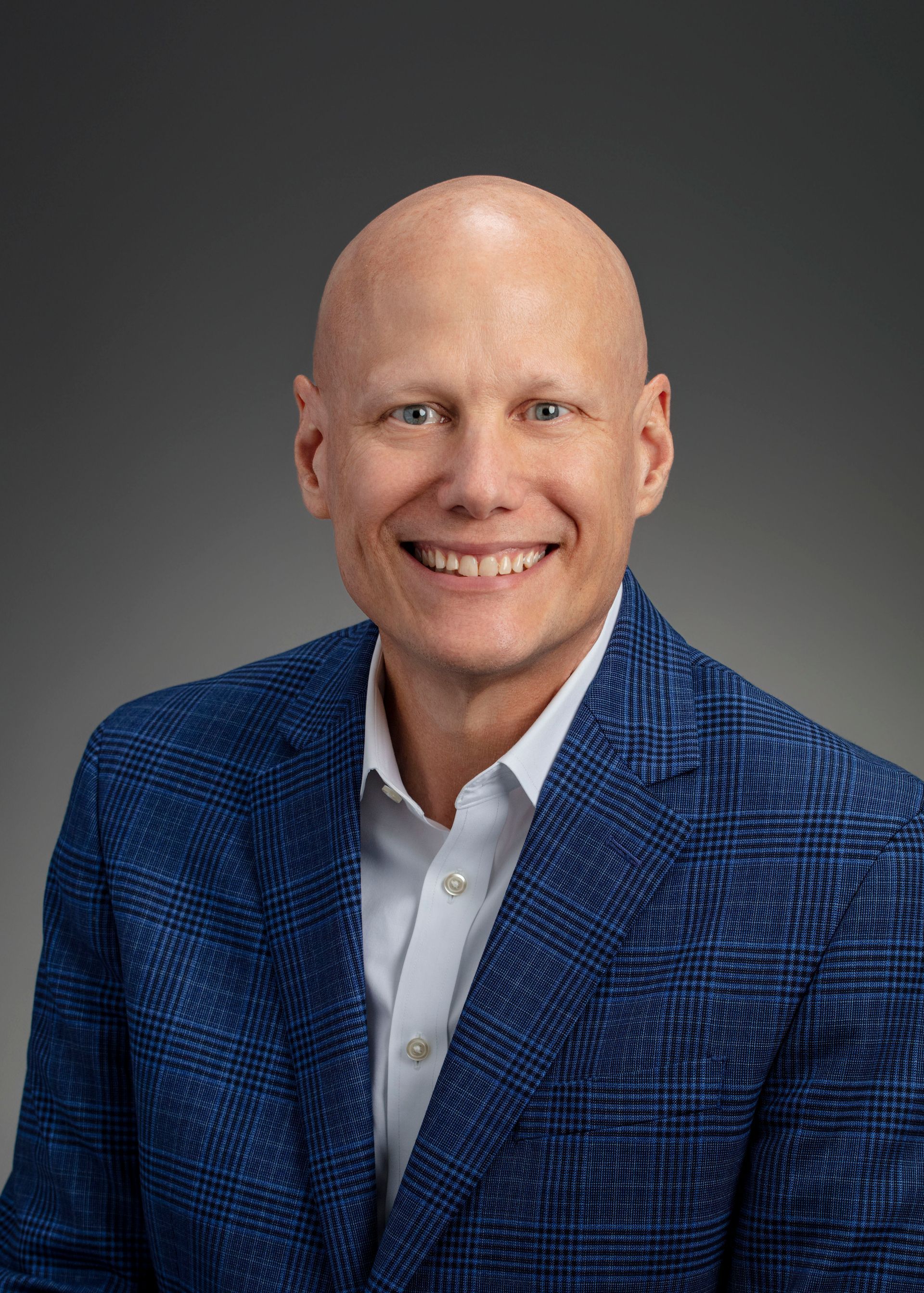 A bald man wearing a blue jacket and white shirt is smiling for the camera.