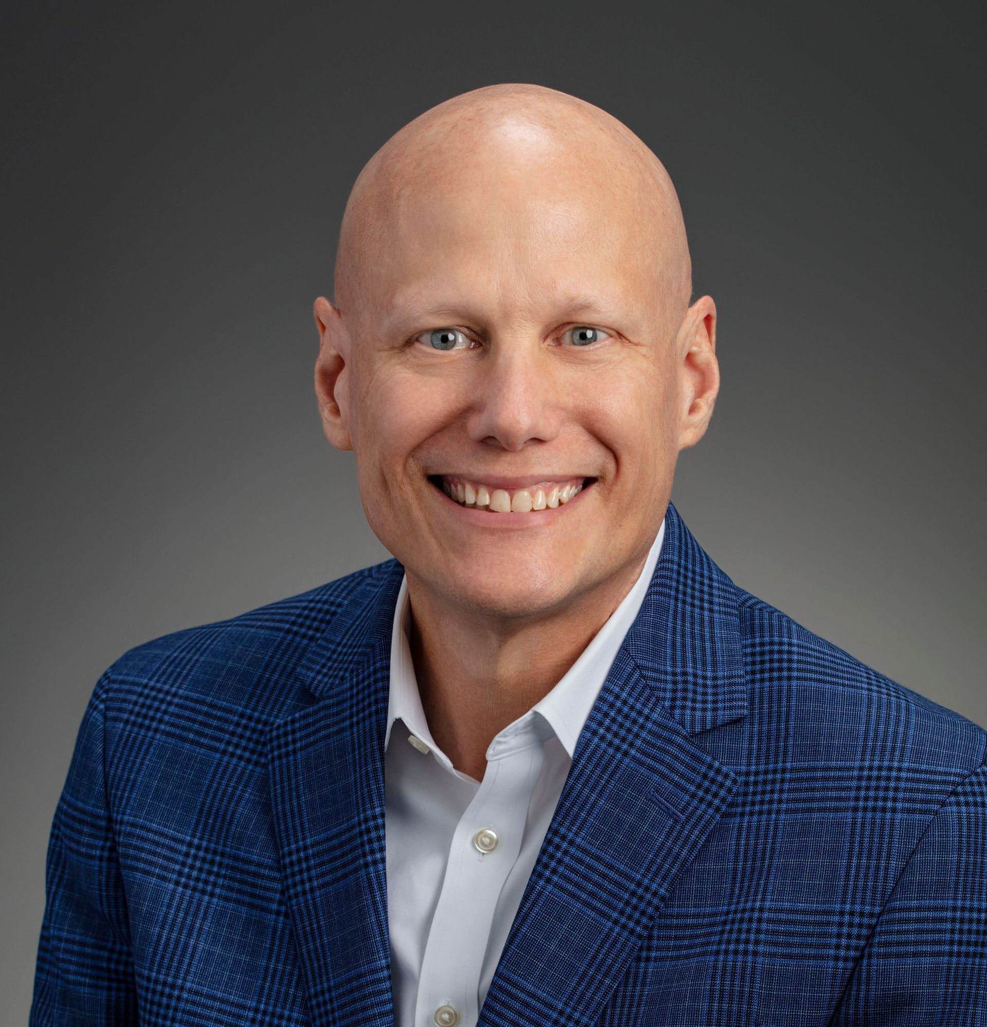 A bald man in a blue suit and white shirt is smiling for the camera.