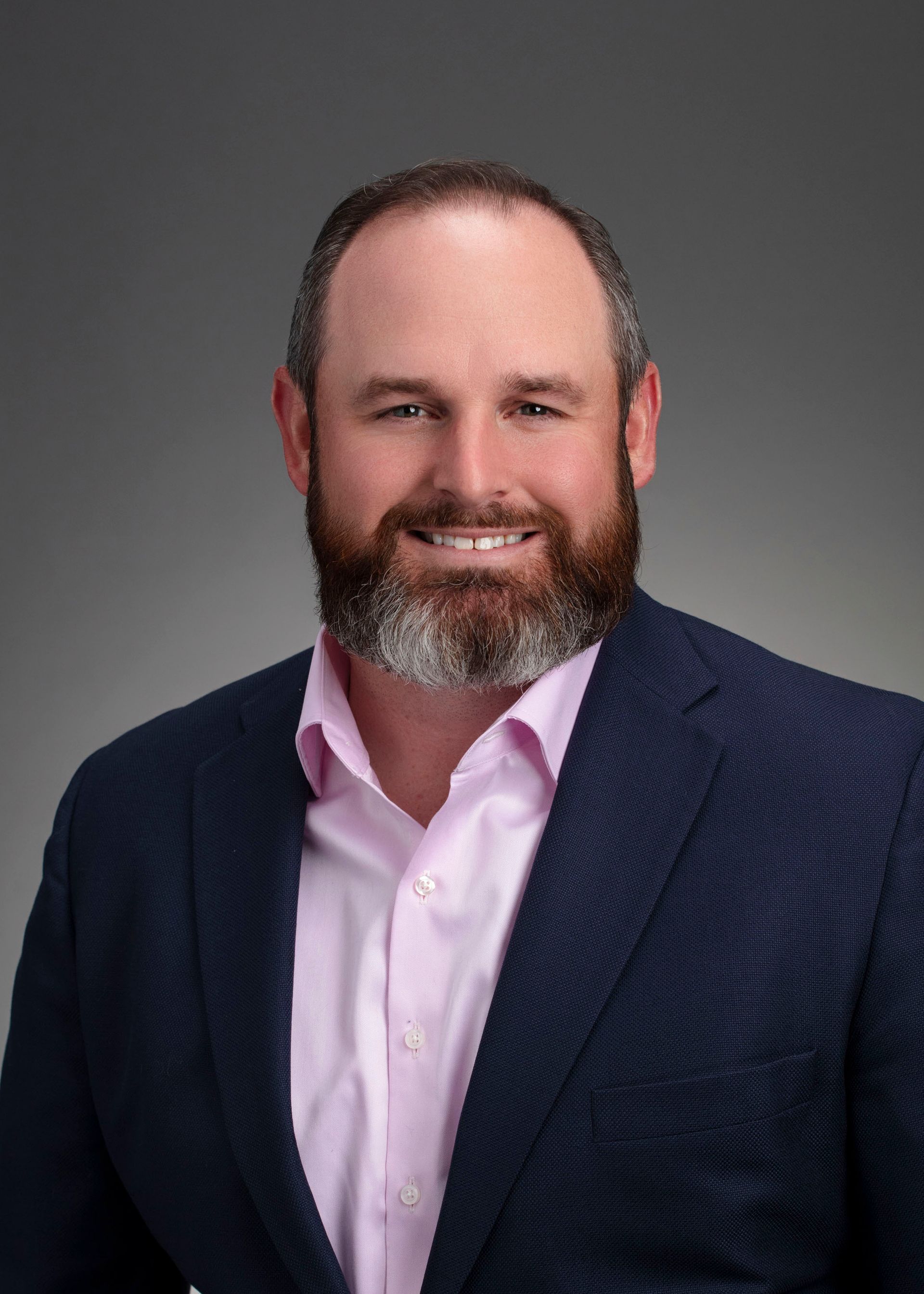 A man with a beard is wearing a blue suit and a pink shirt.