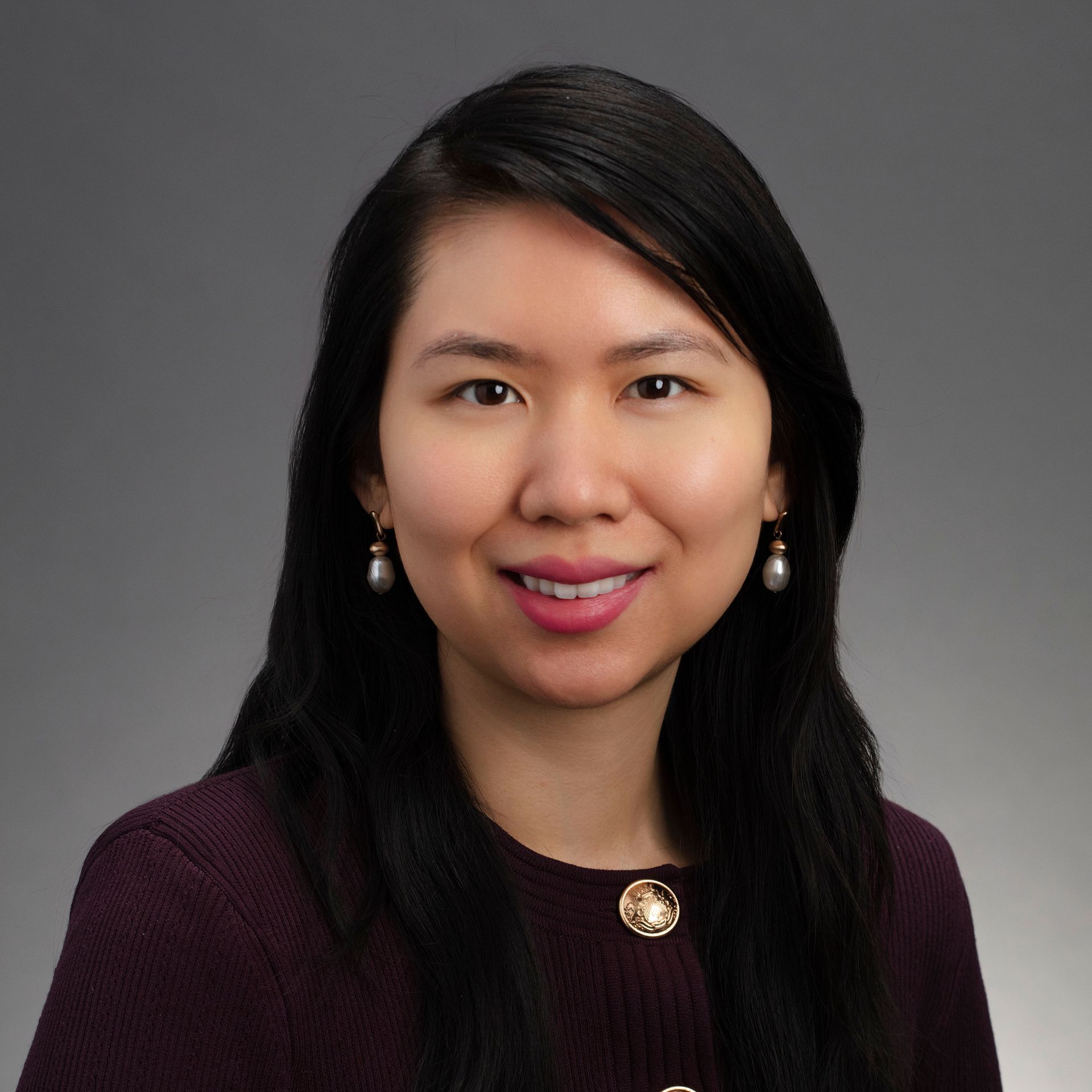 A woman wearing a purple sweater and pearl earrings is smiling for the camera.