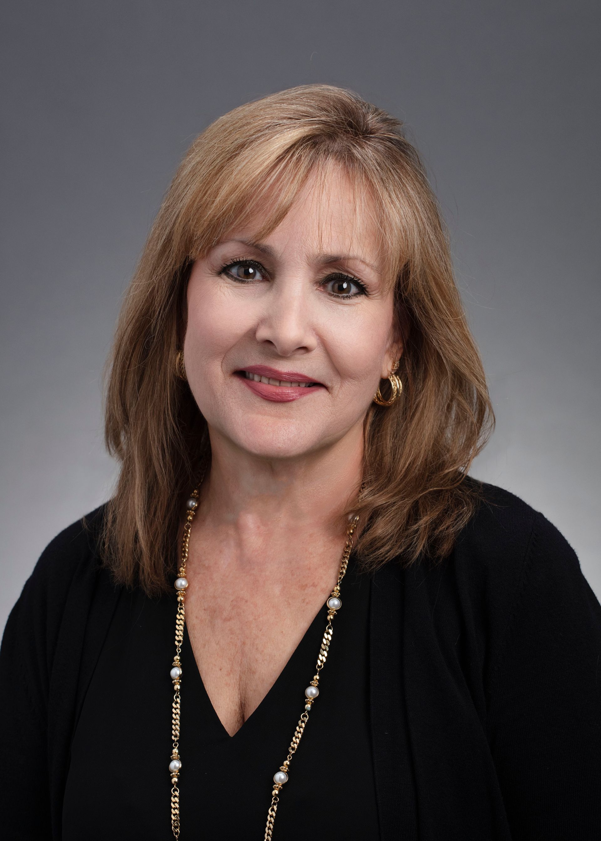 A woman wearing a black shirt and a gold necklace is smiling for the camera.