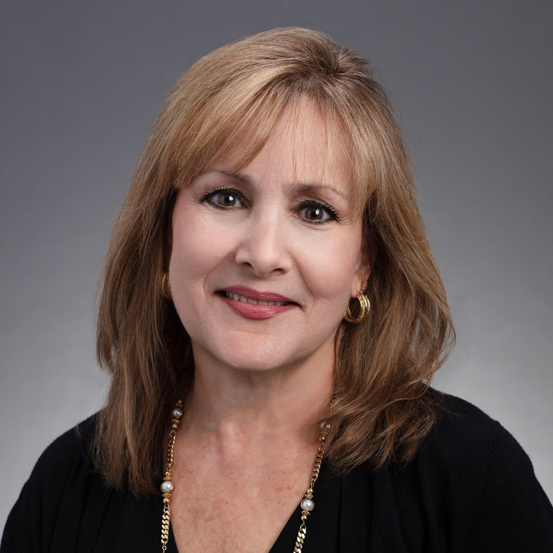 A woman wearing a black shirt and a gold necklace smiles for the camera