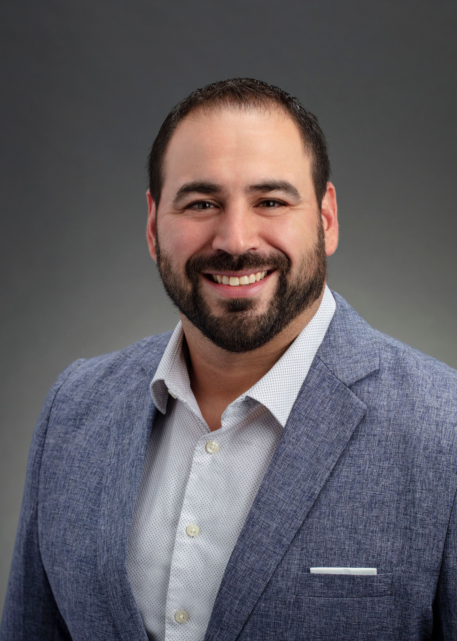 A man with a beard is wearing a blue jacket and smiling for the camera.