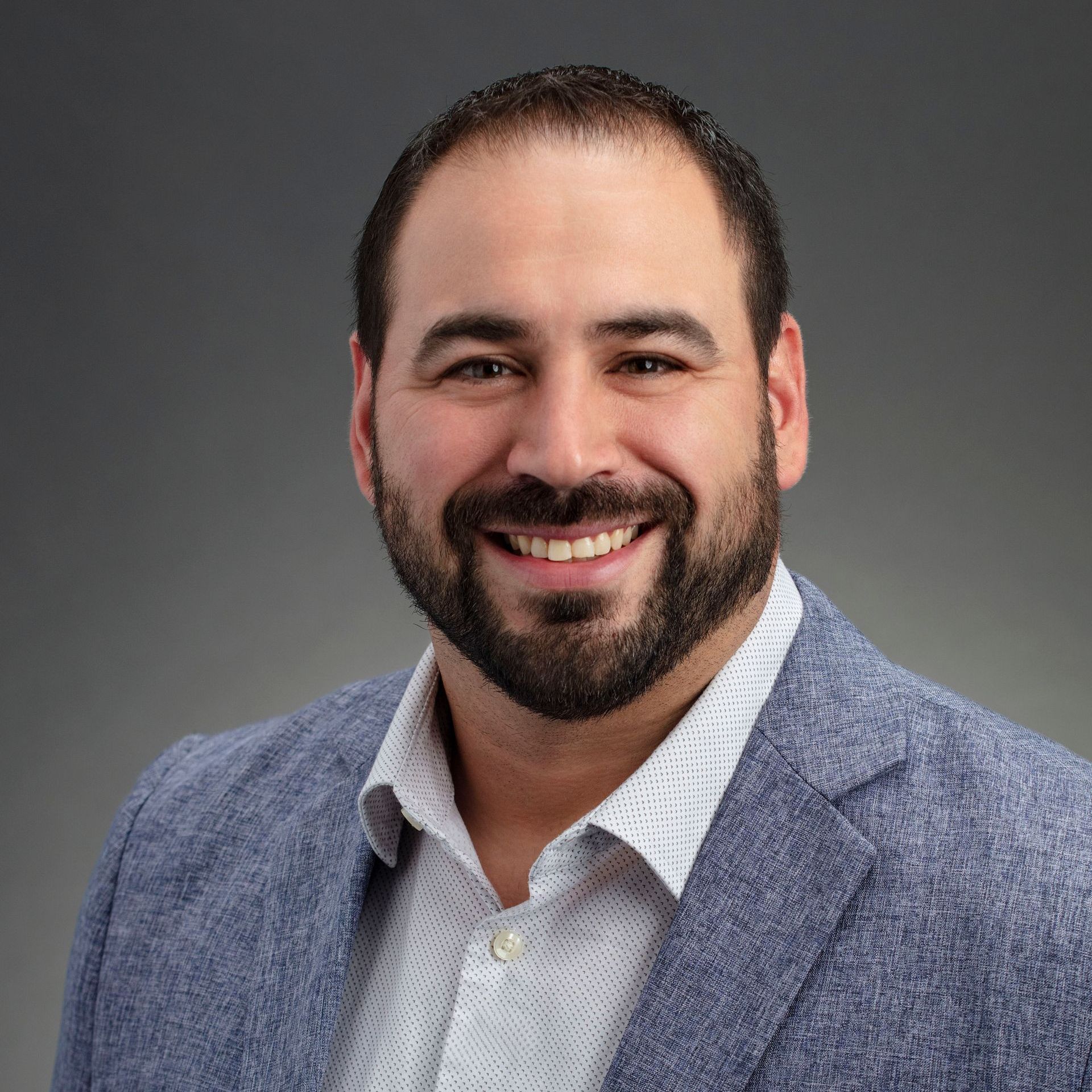 A man with a beard is wearing a blue jacket and smiling for the camera.