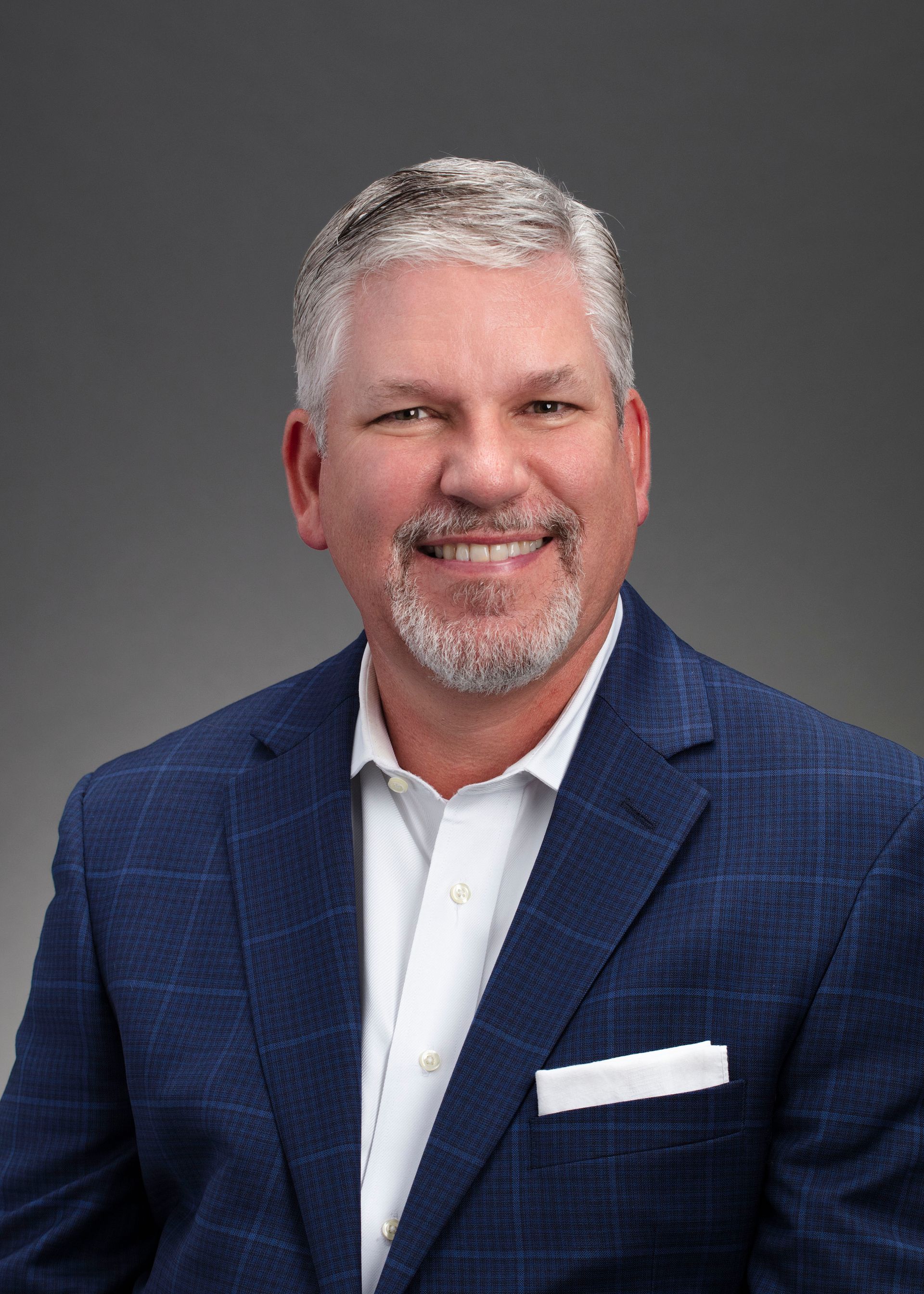 A man in a blue suit and white shirt is smiling for the camera.