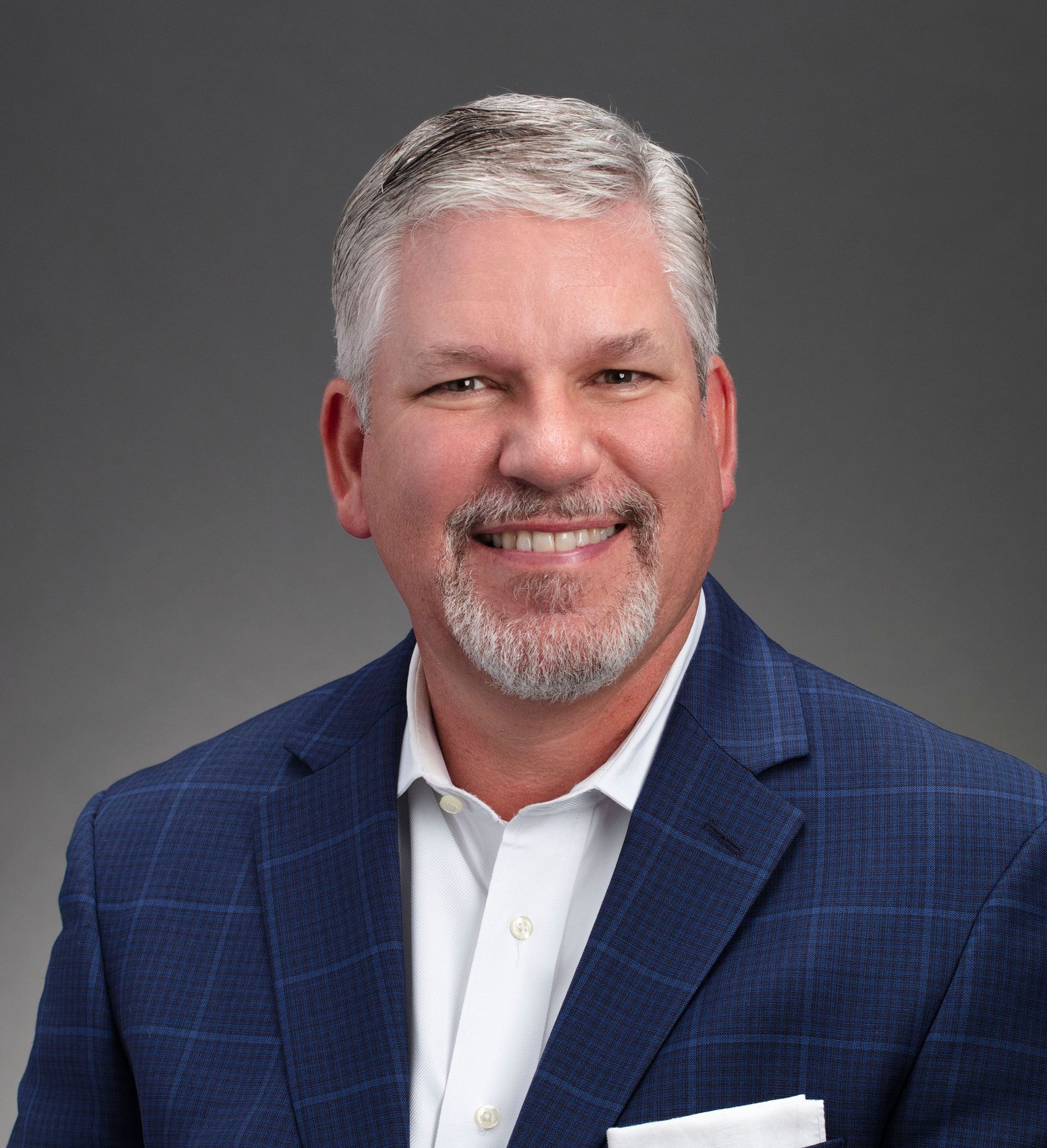 A man in a blue suit and white shirt is smiling for the camera.