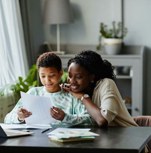 A woman and a child are sitting at a table looking at a piece of paper.