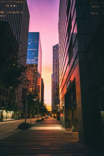 A city street with tall buildings and a sunset in the background.