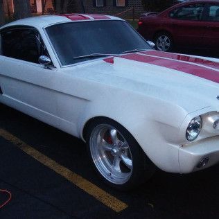 A white mustang with red stripes is parked in a parking lot.