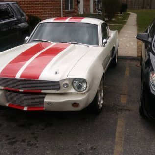 A white mustang with red stripes is parked in a parking lot next to a black car.