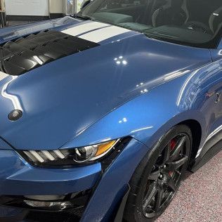 A blue mustang with white stripes on the hood is parked in a garage.