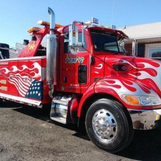 A red tow truck with flames painted on it is parked in front of a house.
