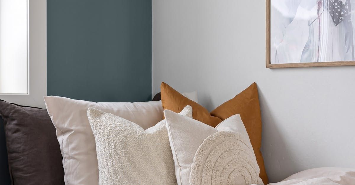 A grouping of pillows on a bed, leaned up against a white wall