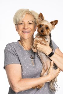 Woman with short blonde hair holds a small Yorkie dog, both smiling, against a white background.