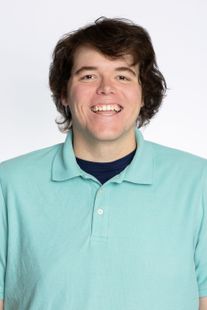 Smiling person with dark curly hair wearing a blue polo shirt.