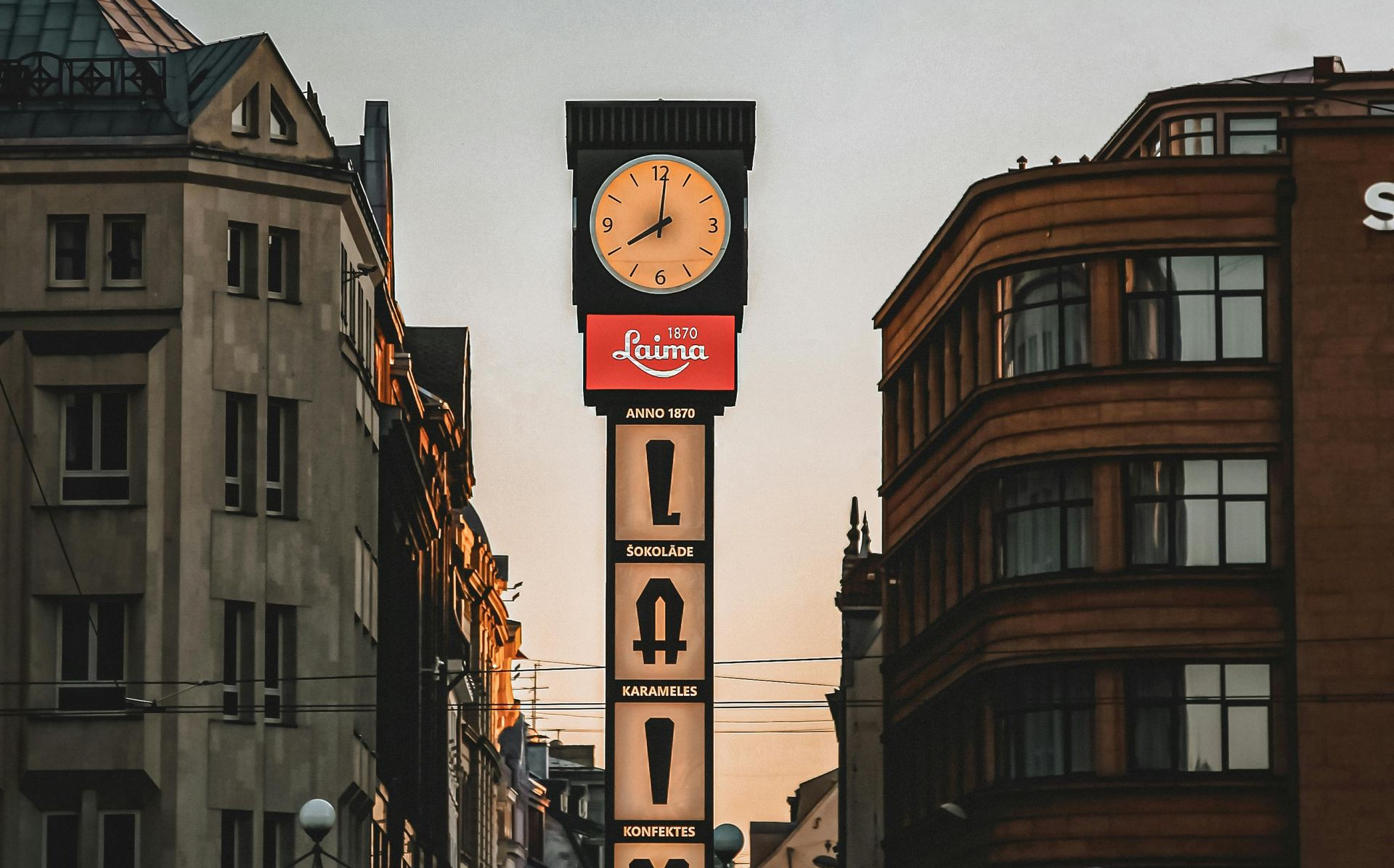 Tall clock tower with clock face, advertisement sign, and letters between buildings.